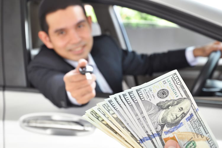 A car salesman extending a key to someone holding a stack of $100 and $20 bills