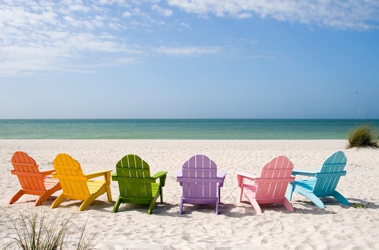 Six beach chairs of different colors set up on a beach