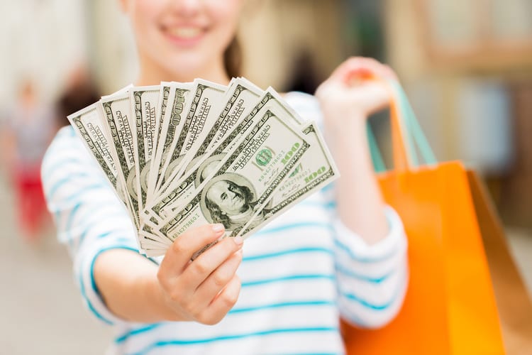 A woman holding up shopping bags and $100 bills