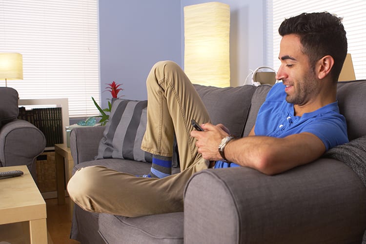 A man reclining on his couch smiling at his phone