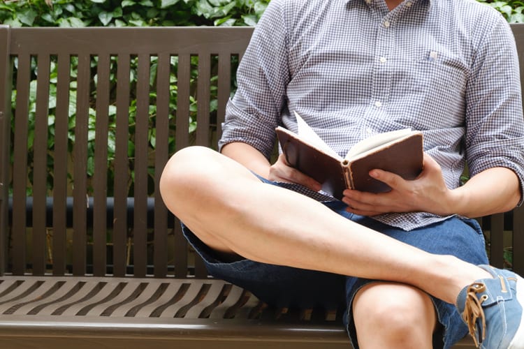 A man in shorts reading a book on a bench