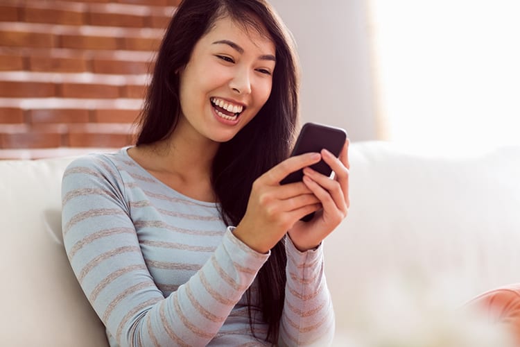 A woman laughing while looking at her phone