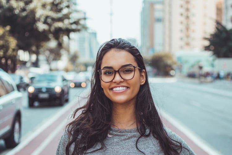 A woman with glasses standing in the middle of a street smiling