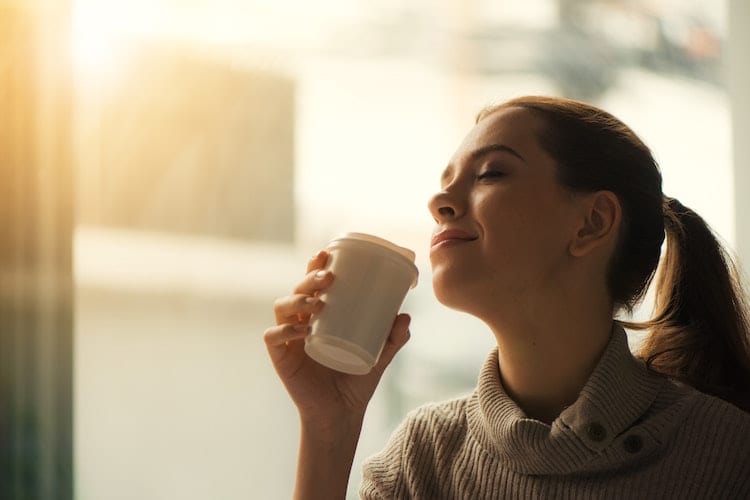 A woman enjoying the smell of her coffee in the morning