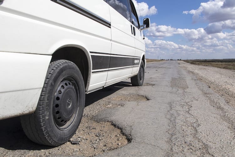 A white van driving through a pothole on a poorly paved road 