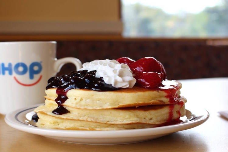 A stack of IHOP pancakes with blueberries, whipped cream, and strawberries on top