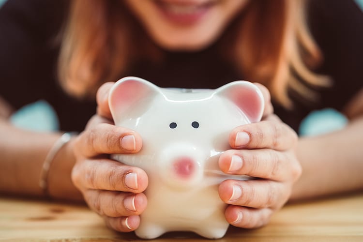 A woman smiling and holding a piggy bank