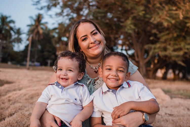 A mother holding two children, both in white polo shirts 