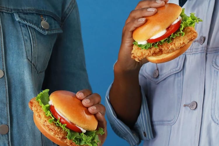 Two people holding fried chicken sandwiches