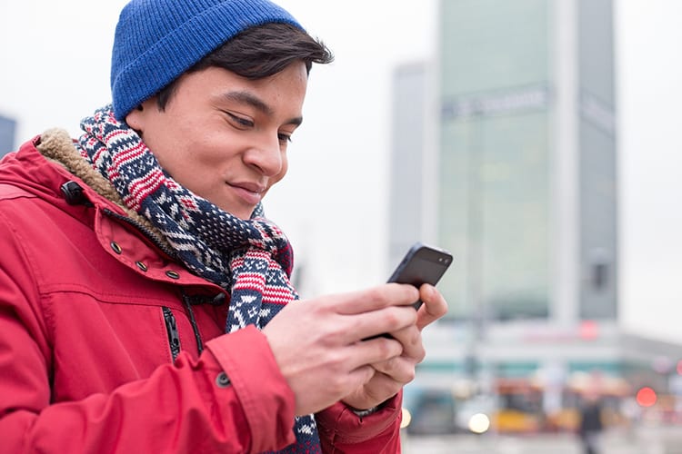 A man in winter clothing outside smiling at his phone