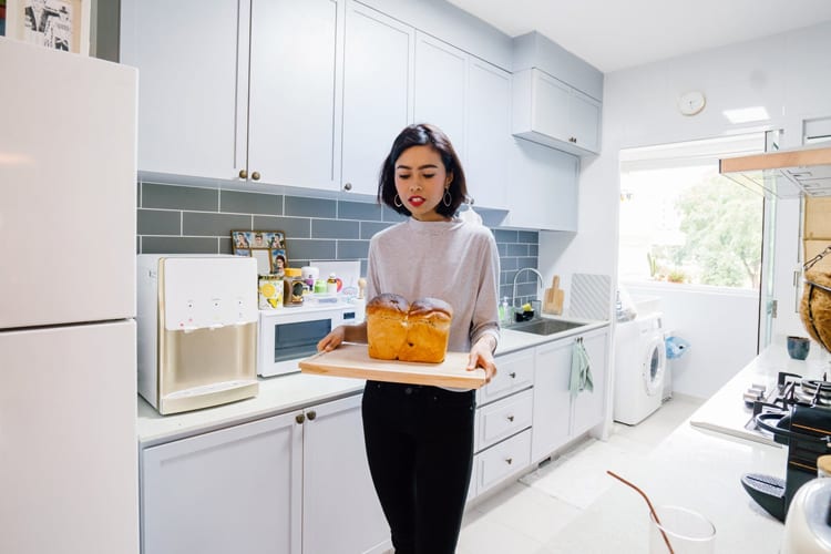 A woman holding a loaf of bread on a cutting board in the kitchen