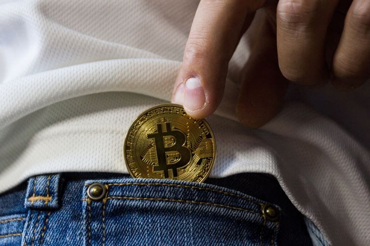 A person dropping a Bitcoin into their jean pocket