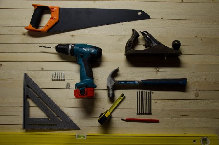 Tools hung in a shed including a drill, saw, hammer, and tape measure 