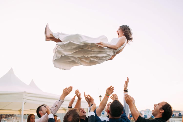 A bride being tossed into the air by her wedding party 