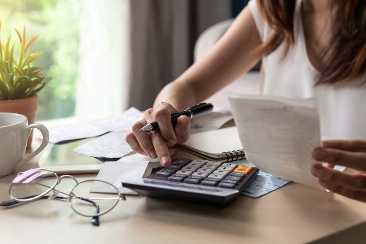 A woman holding a receipt and using a calculator at a coffee table 