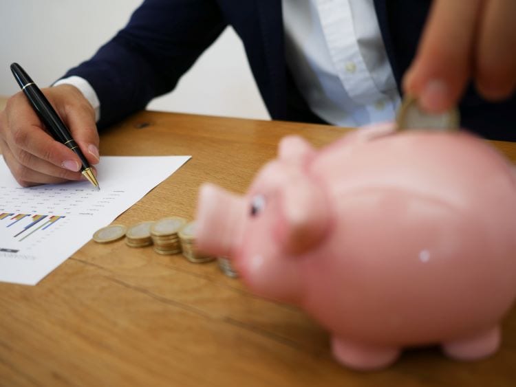 A man writing on a document and putting coins into a piggy bank