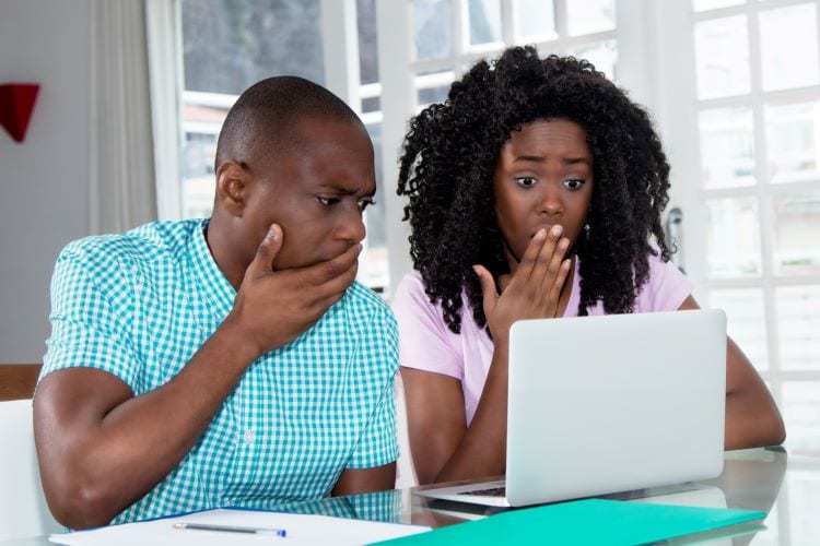 A man and woman looking at a laptop covering their mouths with their hands 