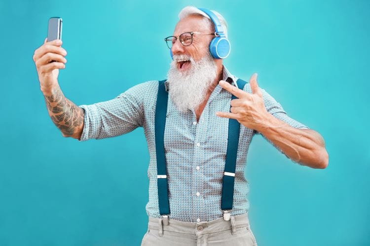 An older man wearing suspenders and headphones smiling for a selfie