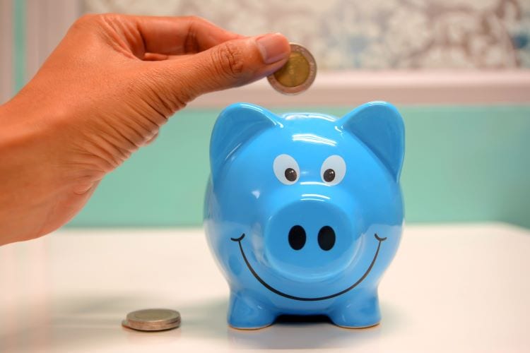 A hand dropping a coin into a blue piggy bank