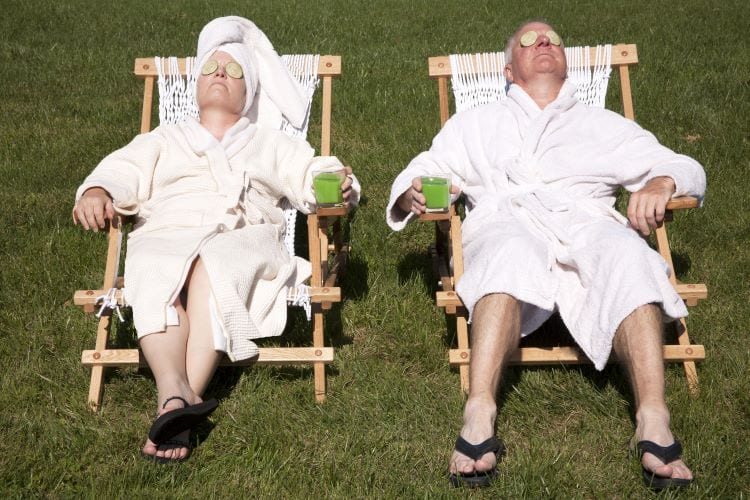 An older couple sitting on lawn chairs, reclining in robes with green drinks