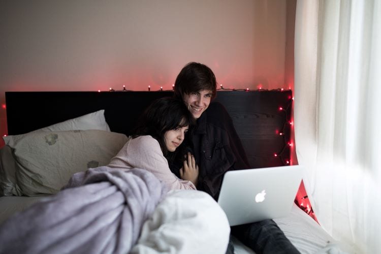 A man and woman watching TV on a laptop together in bed 