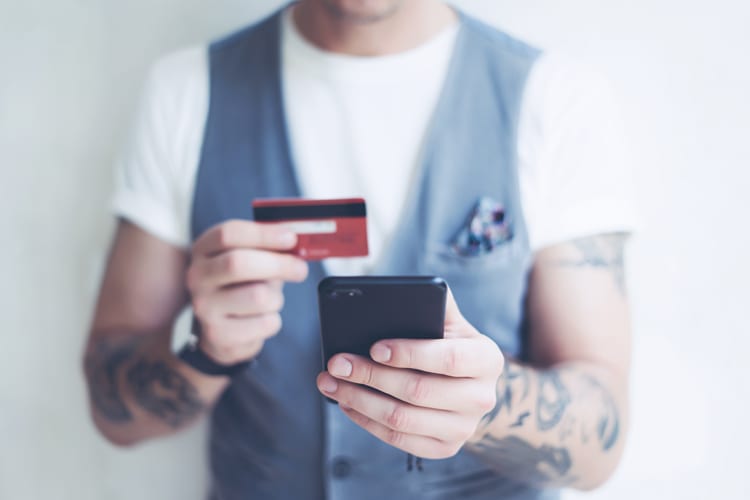 A man with tattoos on his arms holding an iPhone and credit card