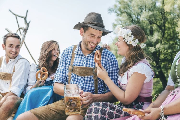 People dressed for Oktoberfest in lederhosen drinking beer and eating pretzels