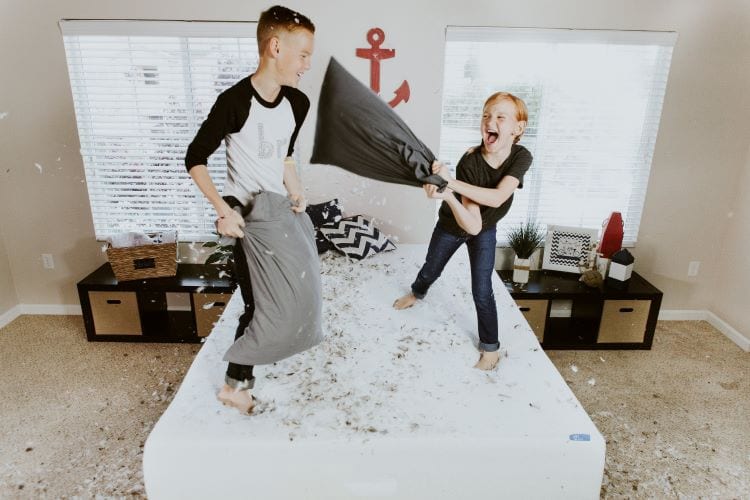 A young boy and girl having a pillow fight standing on a bed