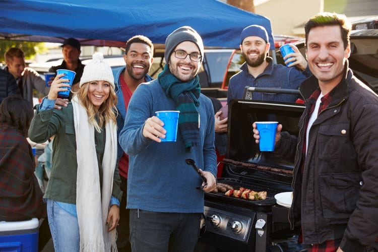 A group of people at a tailgate party, grilling food and drinking from blue solo cups