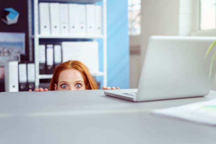 A woman hiding behind her desk and poking her eyes over to see 