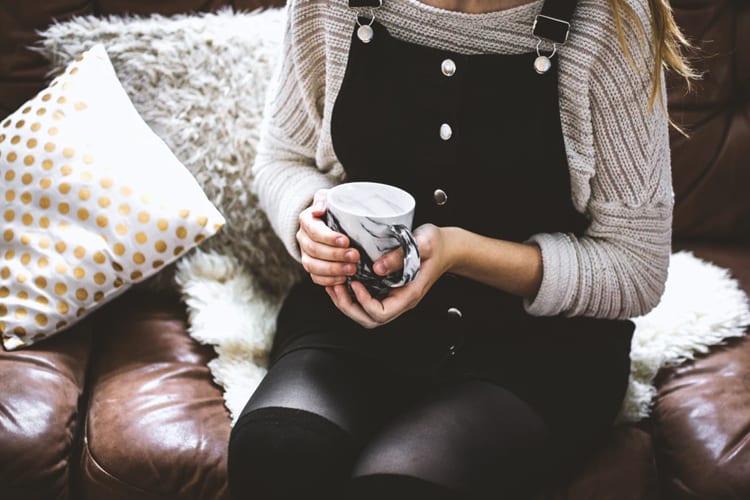 A woman in overalls holding coffee on a couch