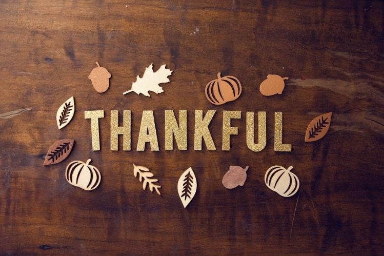 Paper pumpkins, leaves and acorns around the word "thankful" on a wood table