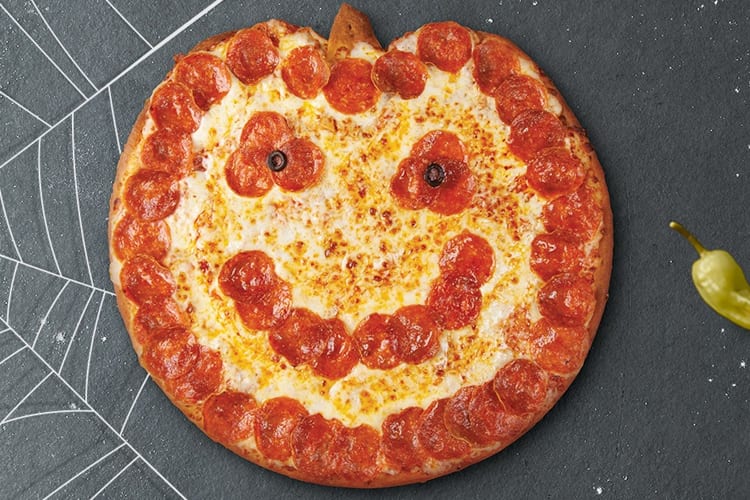A pizza shaped like a pumpkin with pepperoni eyes and mouth