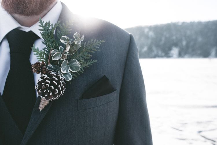 A groom dressed for a winter wedding with snowy ground behind him 