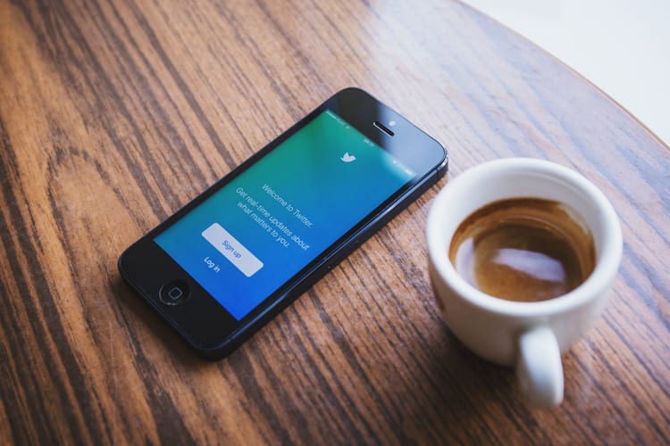 An iPhone with Twitter open next to a cup of coffee