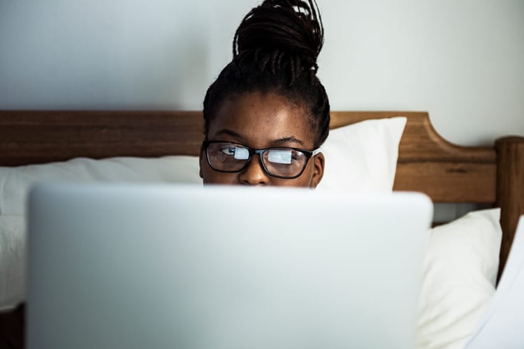 A woman sitting on her bed using her laptop