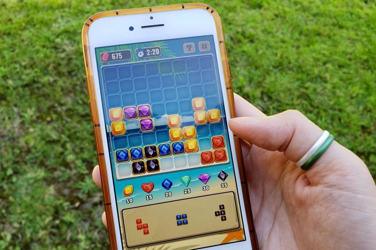Hand holding iPhone 7 with Jewel Blitz game on the display screen