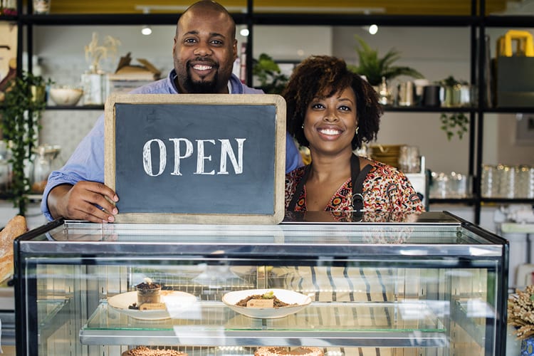 A husband and wife business duo holding an open sign 