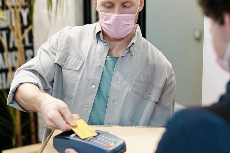 A man with a face mask on tapping his credit card at a store 