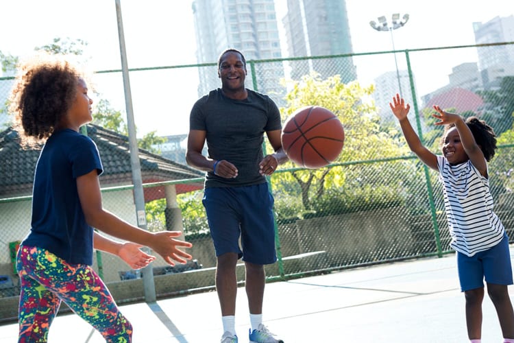 A father playing basketball with his two daughters outside