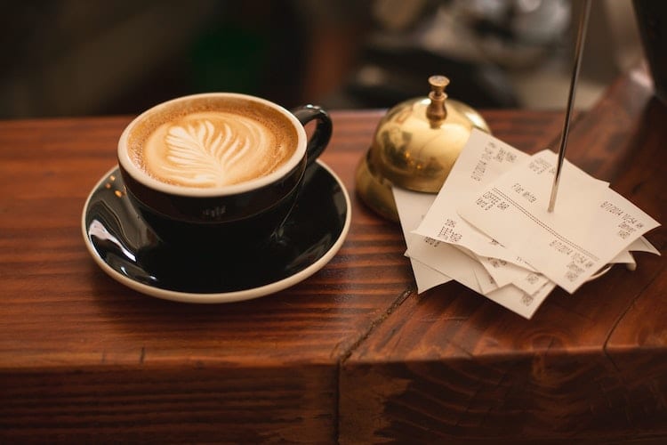A coffee cup next to a stack of receipts and a brass bell