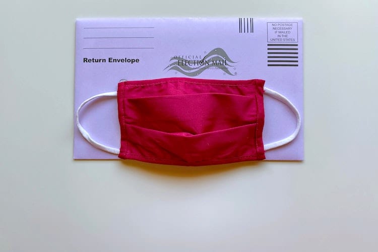 A cloth face mask on top of an absentee ballot envelope