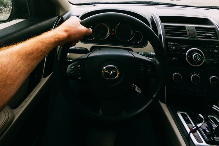 A hand holding the steering wheel of a Mazda car
