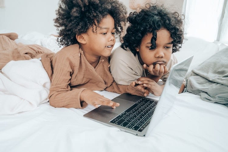 Two young brothers using a laptop in bed