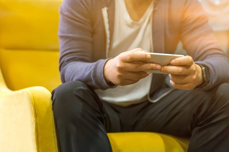 Man playing games on mobile phone sitting on a yellow couch
