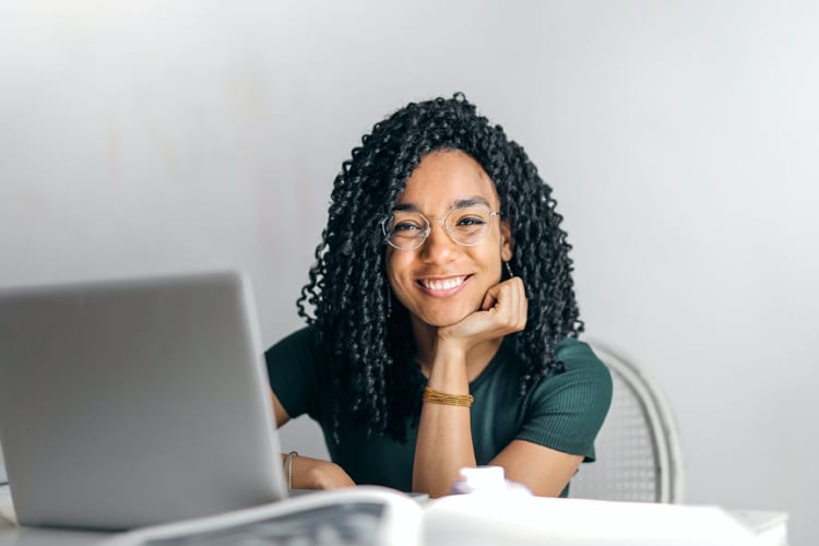 Smiling black woman with glasses sitting in front of laptop