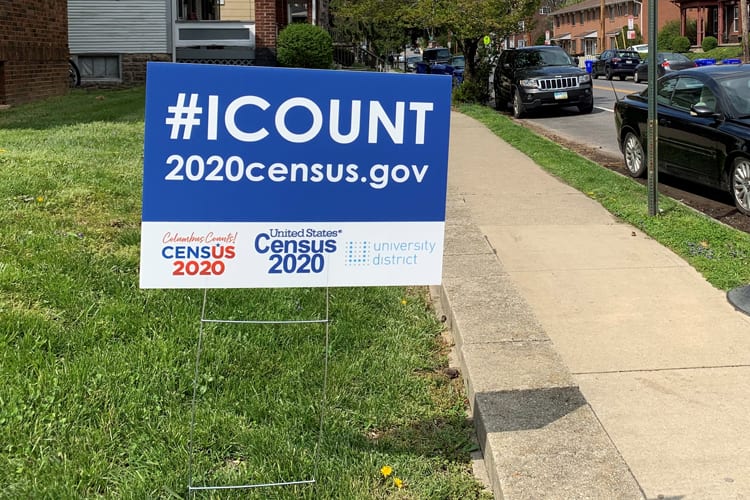 A 2020 census sign stuck in grass next to sidewalk