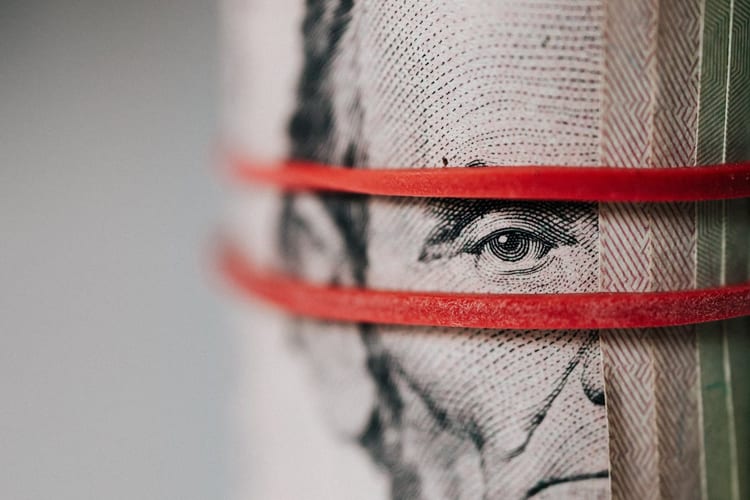 A roll of $5 bills wrapped in red rubberband highlighting Abraham Lincoln's eye