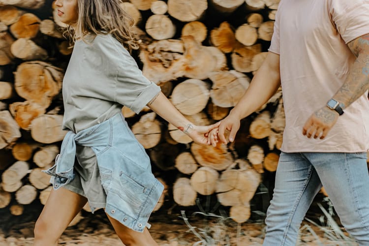 Woman holding hand of boyfriend leading the way in front of a log backdrop