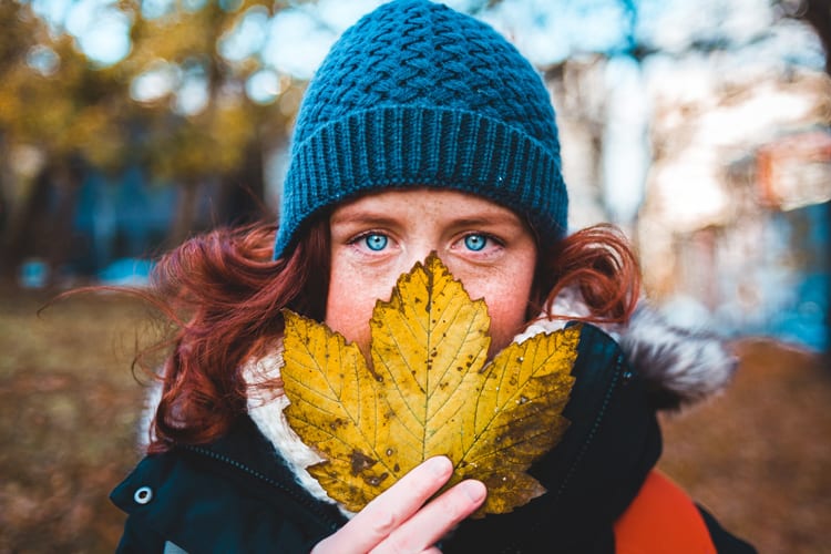 Redhead with blue beanie and blue eyes holding a large yellow maple leaf